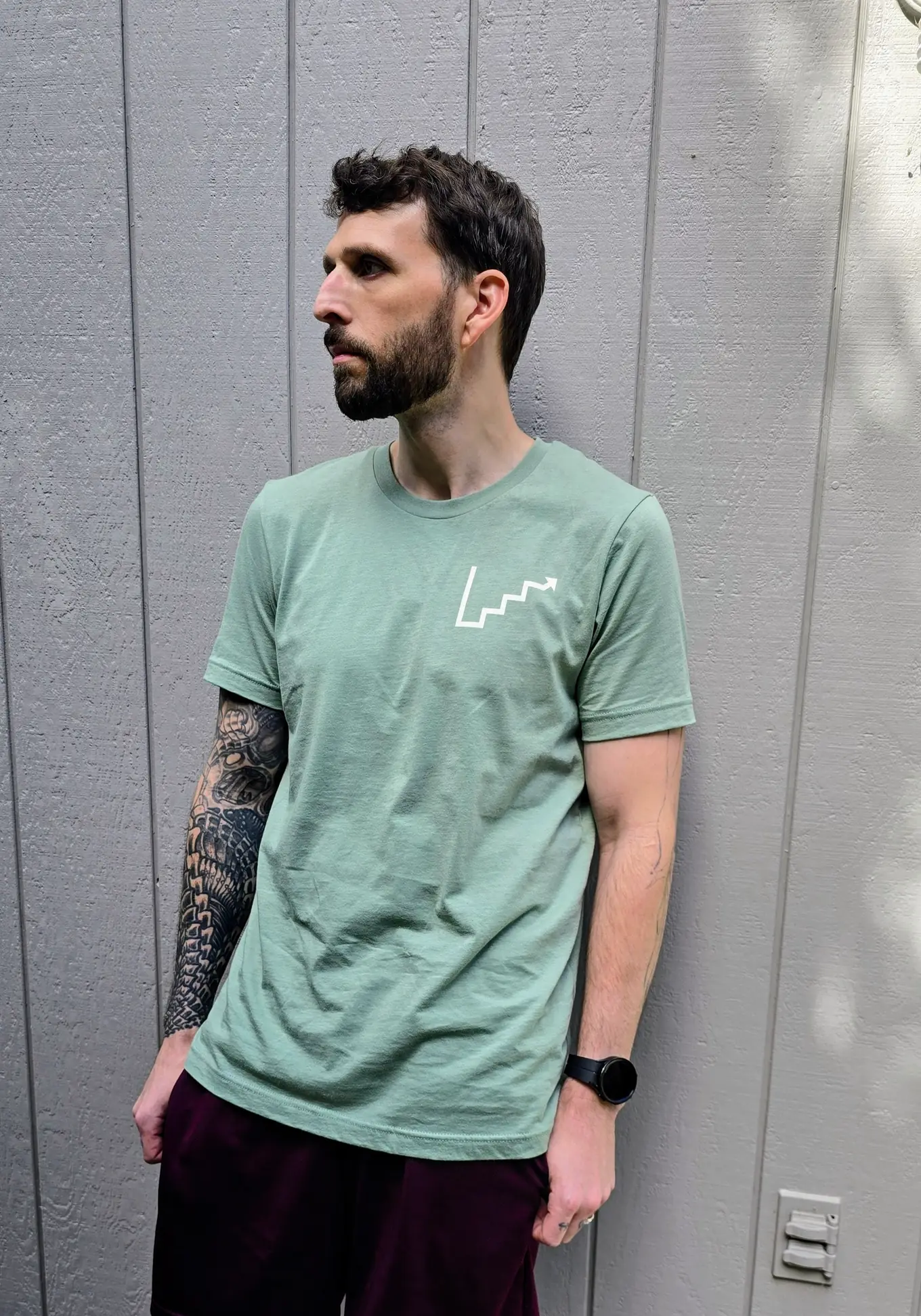 Kenneth wearing the Climb Mark tee in sage, white climb mark on the left chest.